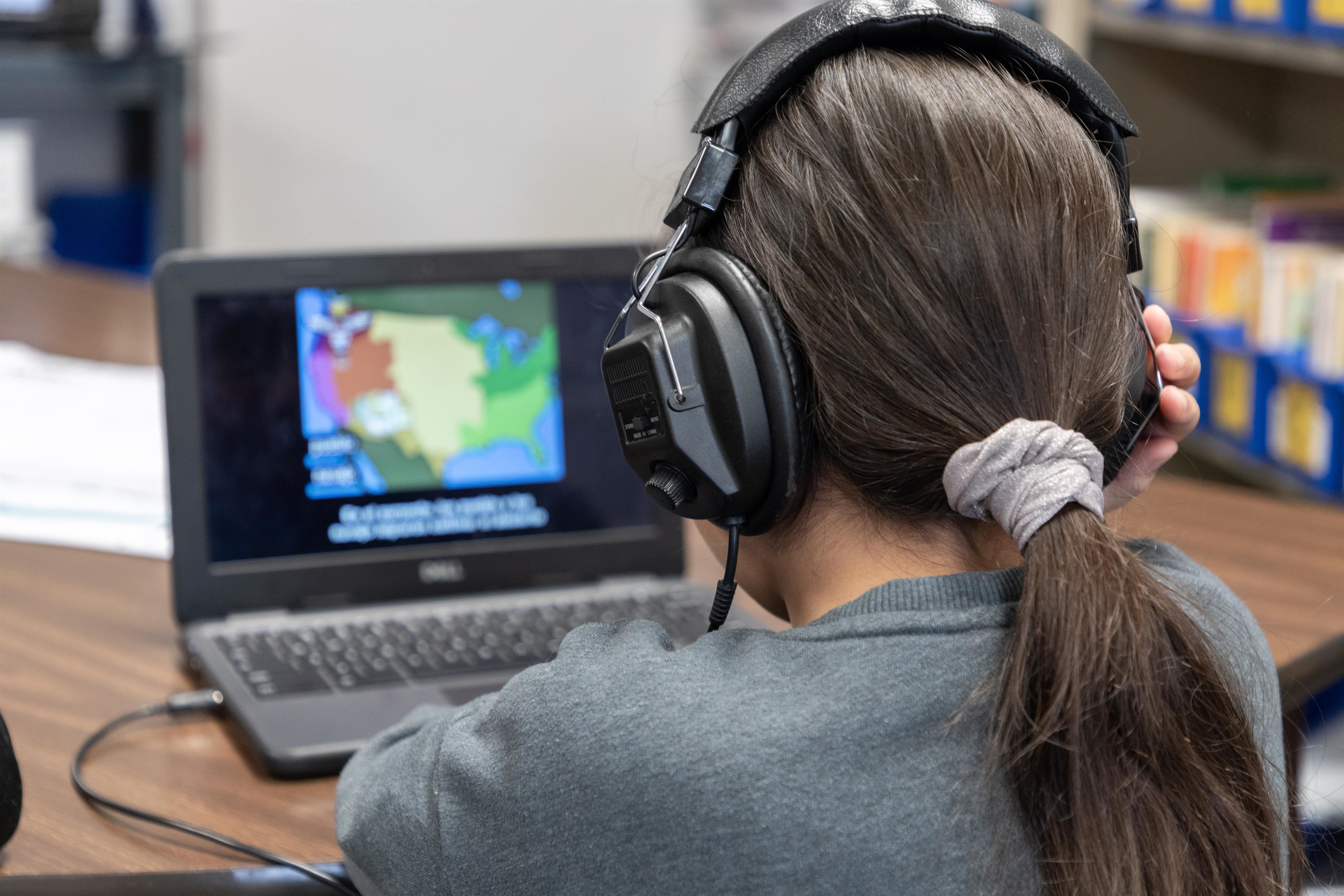Girl with pony tail wearing headphones, staring a computer screen displaying regional map of the United States Girl with pony tail wearing headphones, staring a computer screen displaying regional map of the United States